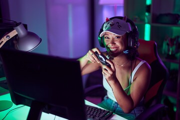 Young beautiful hispanic woman streamer playing video game using joystick at gaming room