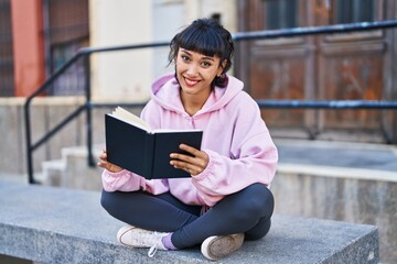Young woman reading book sitting on bench at street