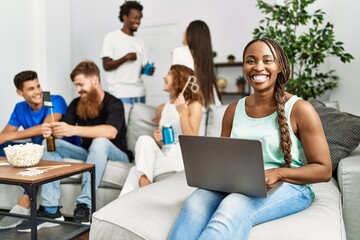 Fototapeta premium Group of young friends smiling happy sitting on the sofa. Woman using laptop at home.