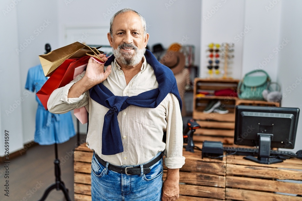 Poster Senior grey-haired man smiling confident holding shopping bags at clothing store