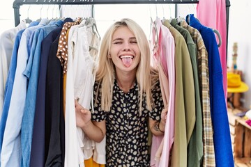 Naklejka na ściany i meble Young blonde woman searching clothes on clothing rack sticking tongue out happy with funny expression.