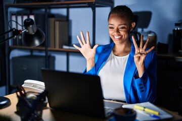 Beautiful african american woman working at the office at night showing and pointing up with fingers number nine while smiling confident and happy.