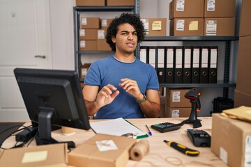 Hispanic man with curly hair working at small business ecommerce disgusted expression, displeased...