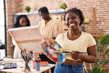 Young black painter woman at art studio holding palette smiling with a happy and cool smile on face. showing teeth.