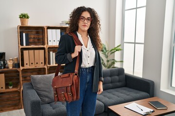 Young hispanic woman at consultation office thinking attitude and sober expression looking self...