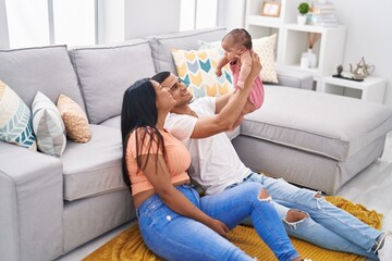 Hispanic family holding baby on air sitting on floor at home