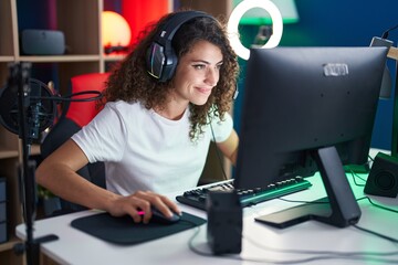 Young beautiful hispanic woman streamer playing video game using computer at gaming room