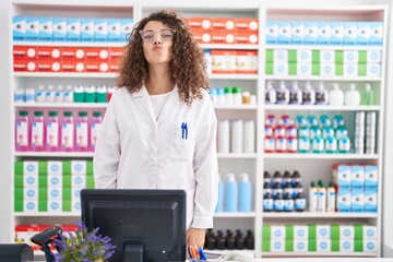 Hispanic woman with curly hair working at pharmacy drugstore looking at the camera blowing a kiss on air being lovely and sexy. love expression.