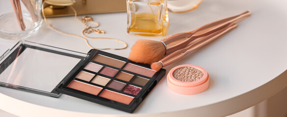 Makeup brushes with cosmetics and perfume on table in room