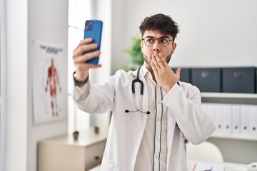 Hispanic man with beard working on online appointment covering mouth with hand, shocked and afraid...