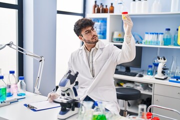 Young hispanic man scientist writing on document holding urine test tube at laboratory