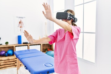 Young caucasian woman wearing physiotherapist uniform using vr glasses at physiotherapy clinic
