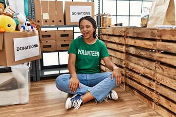 Young african american woman wearing volunteer t shirt at donations stand winking looking at the...