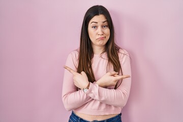 Fototapeta premium Young brunette woman standing over pink background pointing to both sides with fingers, different direction disagree