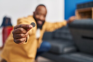 Young african american man holding coin at home - Powered by Adobe