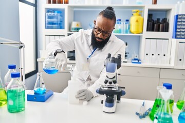 Young african american man wearing scientist uniform measuring liquid at laboratory
