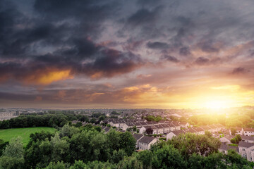 Aerial view on high dense residential area at sunset. House estate by a small park with green trees and fields. Modern family houses with car park and backyard. Galway, Ireland.