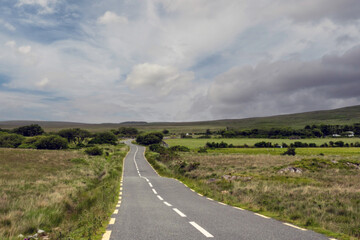 Small country road in Ireland. Green agriculture land on each side. Blue cloudy sky Transportation industry. Irish country side landscape.