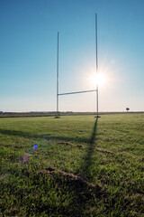 Fototapeta na wymiar Field with tall goal posts for Irish National sports on green grass against clear blue sky and the sun. Rugby, hurling, camogie and Gaelic football training ground. Nobody. Popular sport in Ireland.