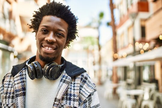 Handsome black man with afro hair wearing headphones smiling happy outdoors