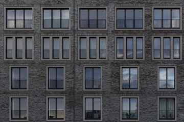 fragment of facade of building with windows. Facing with black brick. Two- and three-leaf windows on gray brick facade. Architectural background