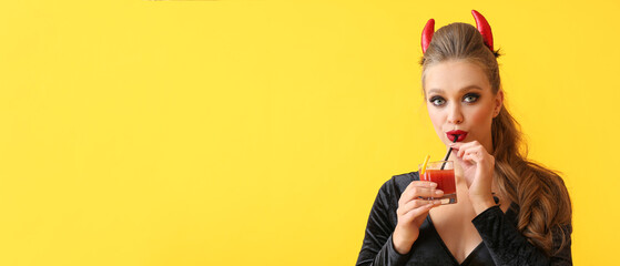 Sexy young woman dressed for Halloween party drinking cocktail on yellow background with space for...