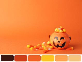 Basket with tasty candy corns for Halloween on orange background. Different color patterns