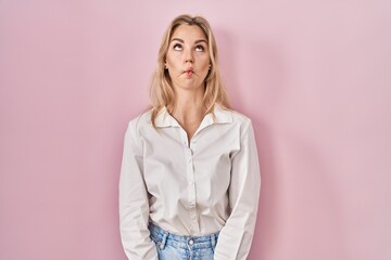 Young caucasian woman wearing casual white shirt over pink background making fish face with lips, crazy and comical gesture. funny expression.