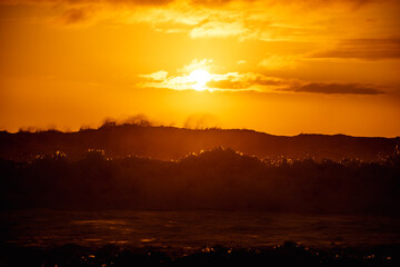 Fototapeta premium paisaje de ocaso en la playa con silueta del sol sobre el mar con olas reventando en la orilla con cielo anaranjado