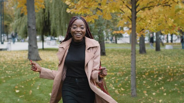 Active energetic positive joyful woman dancing in autumn park having fun young attractive satisfied african girl moves to music outdoors performing funny dance rejoices in success good mood concept