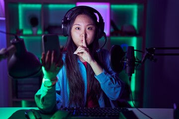 Young asian woman playing video games with smartphone asking to be quiet with finger on lips. silence and secret concept.