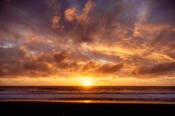 Fototapeta na wymiar Paisaje de atardecer en la playa con ocaso en el mar y nubes iluminadas por el sol