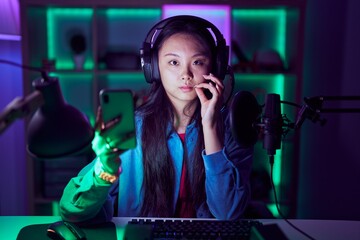 Young asian woman playing video games with smartphone mouth and lips shut as zip with fingers. secret and silent, taboo talking