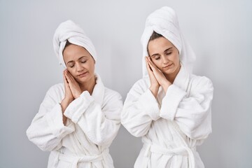 Middle age woman and daughter wearing white bathrobe and towel sleeping tired dreaming and posing with hands together while smiling with closed eyes. - obrazy, fototapety, plakaty