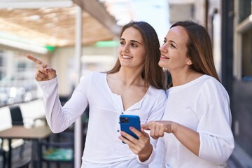 Two women mother and daughter using smartphone at street