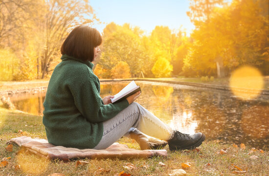 Young woman reading book near pond in autumn park