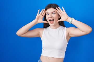 Fototapeta na wymiar Young caucasian woman standing over blue background smiling cheerful playing peek a boo with hands showing face. surprised and exited