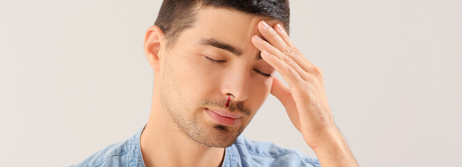 Young man with nosebleed on light background