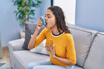 Young african american woman using inhaler sitting on sofa at home