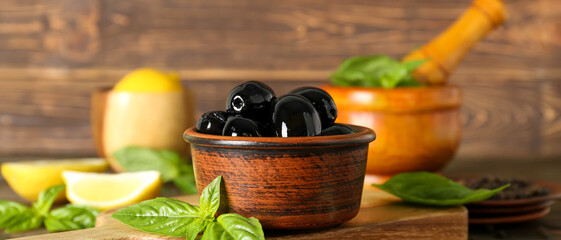 Bowl of tasty black olives on wooden table