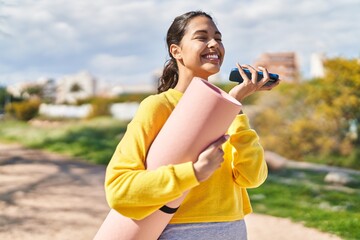 Young african american woman talking on the smartphone holding yoga mat at park