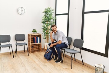 Young hispanic man talking on the smartphone sitting on chair at waiting room