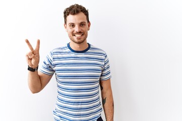 Handsome young man standing over isolated background showing and pointing up with fingers number two while smiling confident and happy.