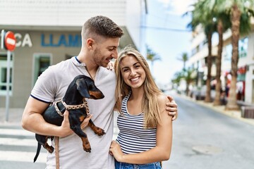 Young caucasian couple hugging and smiling happy standing with dog at the city.