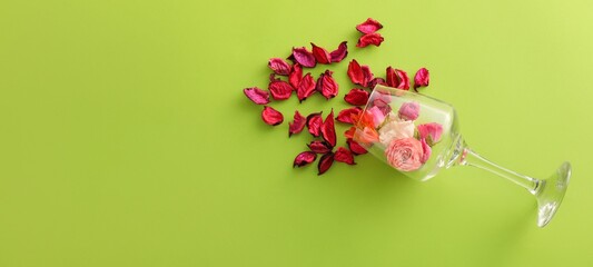 Overturned wine glass with flowers and petals on green background