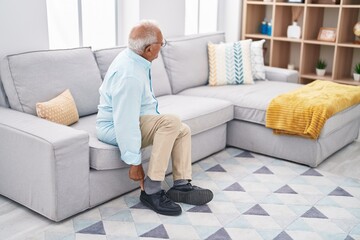 Senior grey-haired man suffering for feet pain sitting on sofa at home