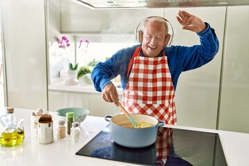 Senior man listening to music cooking spaghetti at kitchen