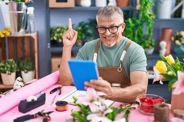 Hispanic man with grey hair working at florist shop doing video call with tablet smiling with an idea or question pointing finger with happy face, number one