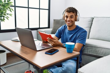 Young hispanic man using laptop and touchpad device at home