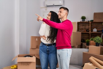 Man and woman couple standing together pointing with finger to the side at new home